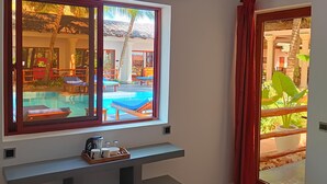 A hotel room with a large window, a ceiling fan, a flat-screen TV, a wooden bench, and a small table with a tray of items.