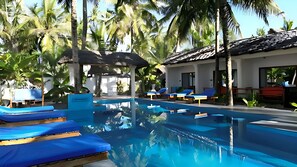 A pool area with blue lounge chairs, a clear pool, and palm trees.