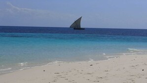 A beach with clear turquoise waters and a sailboat in the distance.