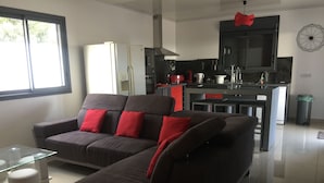 A modern living room with a sectional sofa, a glass coffee table, and a kitchen area with a built-in island. - Profiter de L'extèrieur Avec Cette Villa (Saint-Louis)