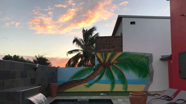 A swimming pool with a waterfall feature, a mural of a palm tree, and lounge chairs. - Profiter de L'extèrieur Avec Cette Villa (Saint-Louis)