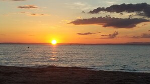 Ein Sonnenuntergang über einem ruhigen Meer mit einem Strand im Vordergrund.
