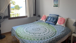 A bedroom with a bed, a window with curtains, a wall-mounted lamp, a bedside table, and a poster. - 3 Bedroom Villa, San Jaime, Son Bou (Son Bou)