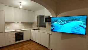 A modern kitchen with white cabinets, a built-in oven, and a large flat-screen TV mounted on the wall displaying a scenic view. - 3 Bedroom Villa, San Jaime, Son Bou (Son Bou)