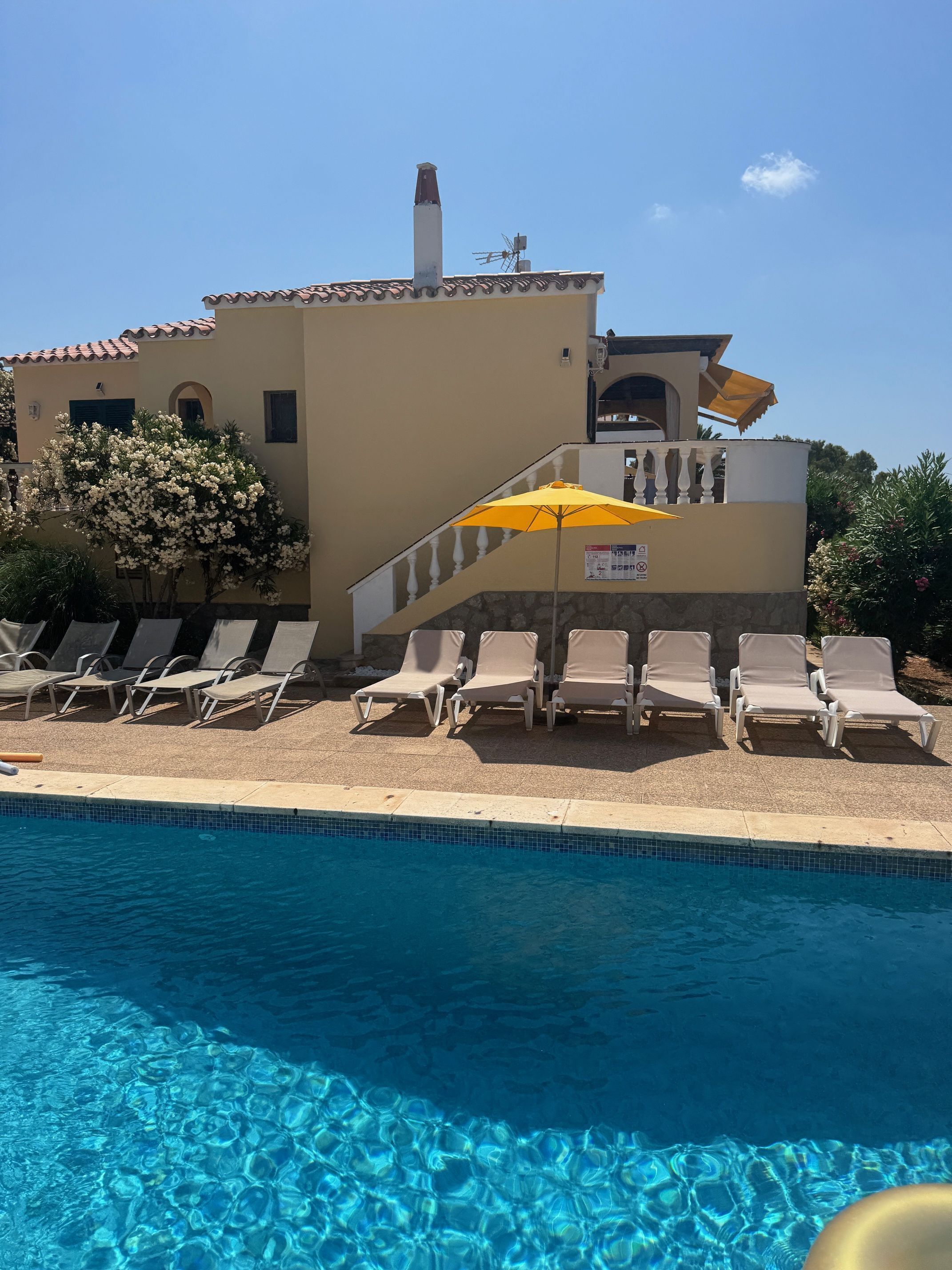 Une piscine avec des chaises longues et un parasol jaune.