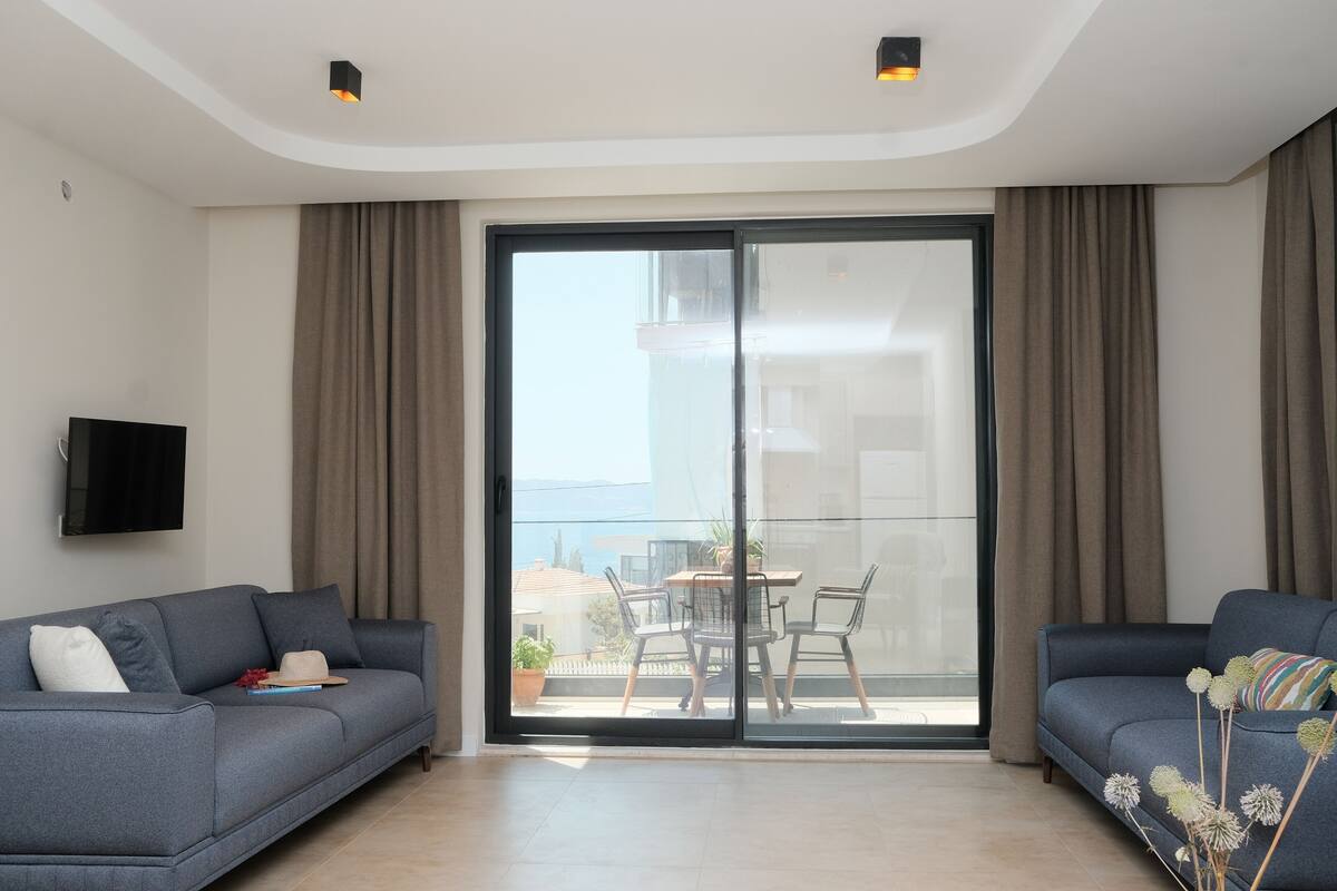 A modern living room with a sofa, a TV, and a balcony with a table and chairs.