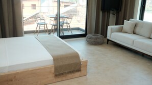 A modern hotel room with a large bed, a sofa, a TV, and a balcony with a table and chairs. - Kaktus Suites Hotel (Kas)