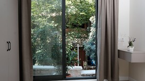 A room with a sliding glass door leading to a garden area, a small white table with a vase, and a cabinet with black handles. - Kaktus Suites Hotel (Kas)