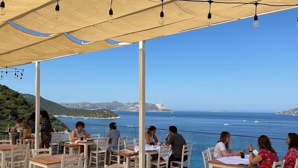 An outdoor dining area with tables and chairs, overlooking a coastal view with boats and hills. - Kaktus Suites Hotel (Kas)