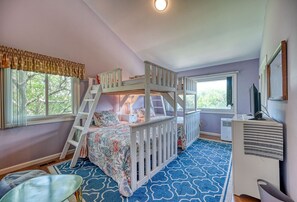 Quarto de criança com beliches, escrivaninha e janela com cortinas.