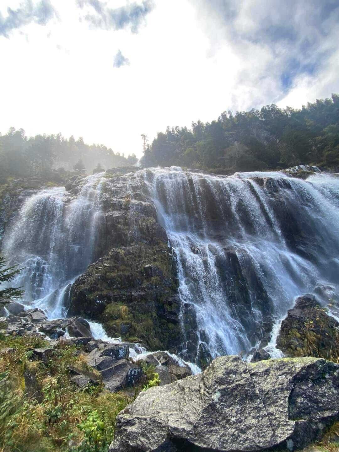A waterfall cascading over rocky terrain with lush greenery in the background.