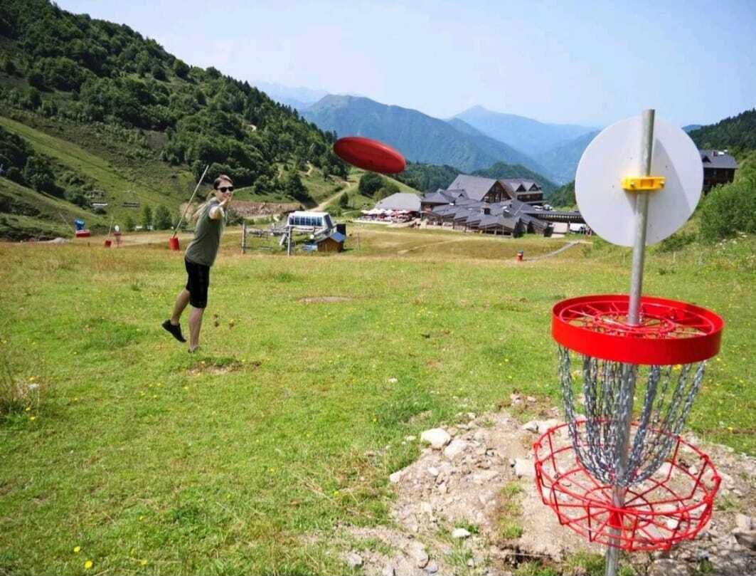Una persona lanza un disco en un campo cubierto de hierba, con un cesto de disc golf al frente.
