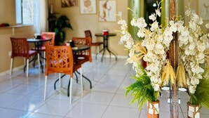 A dining area with a wooden ceiling, tiled floor, and a central table with chairs. There are potted plants and framed artwork on the walls. - Pousada do Trinta (Fernando de Noronha)