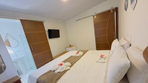 A hotel room with a bed, a bedside table, a TV, a bathroom, and a shower area. - Pousada do Trinta (Fernando de Noronha)