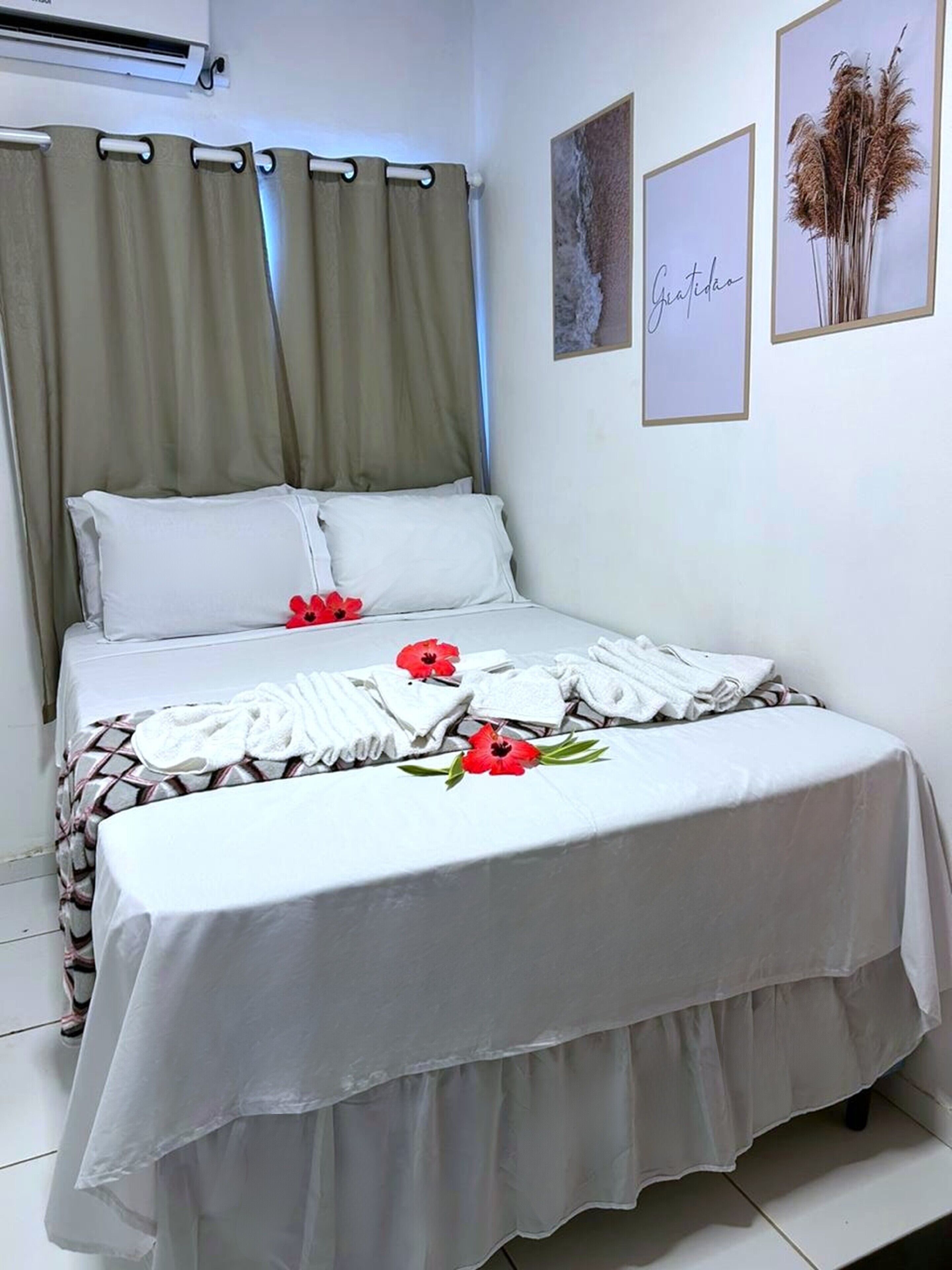 A neatly made bed with white linens and red flowers, a grey curtain, and two framed pictures on the wall.