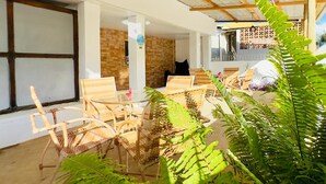 An outdoor seating area with wicker furniture, a glass table, and a hanging light fixture. - Pousada do Trinta (Fernando de Noronha)