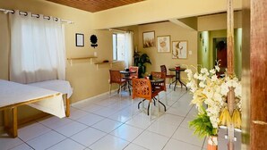 A room with a wooden ceiling, a bed, a dining area with chairs and a table, and a vase with flowers. - Pousada do Trinta (Fernando de Noronha)