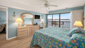 A bedroom with a bed, dresser, and a large window with a view.