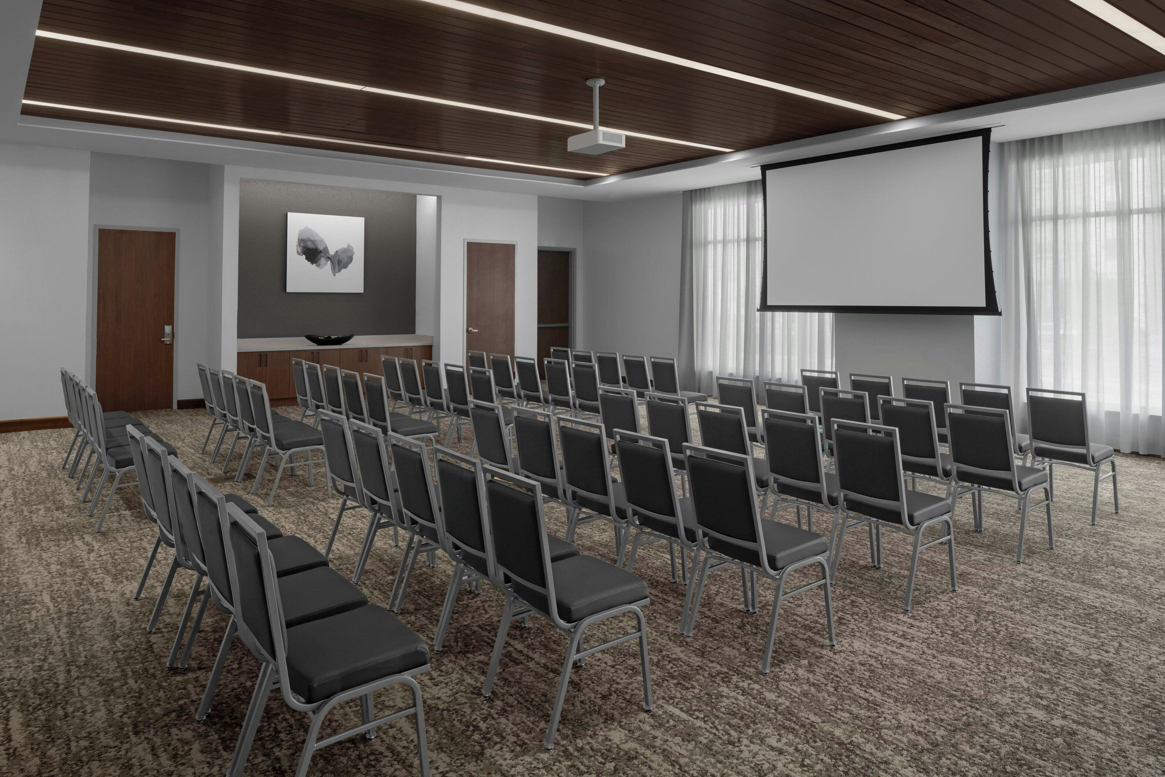 A conference room with rows of chairs, a projector screen, and a large window with curtains.