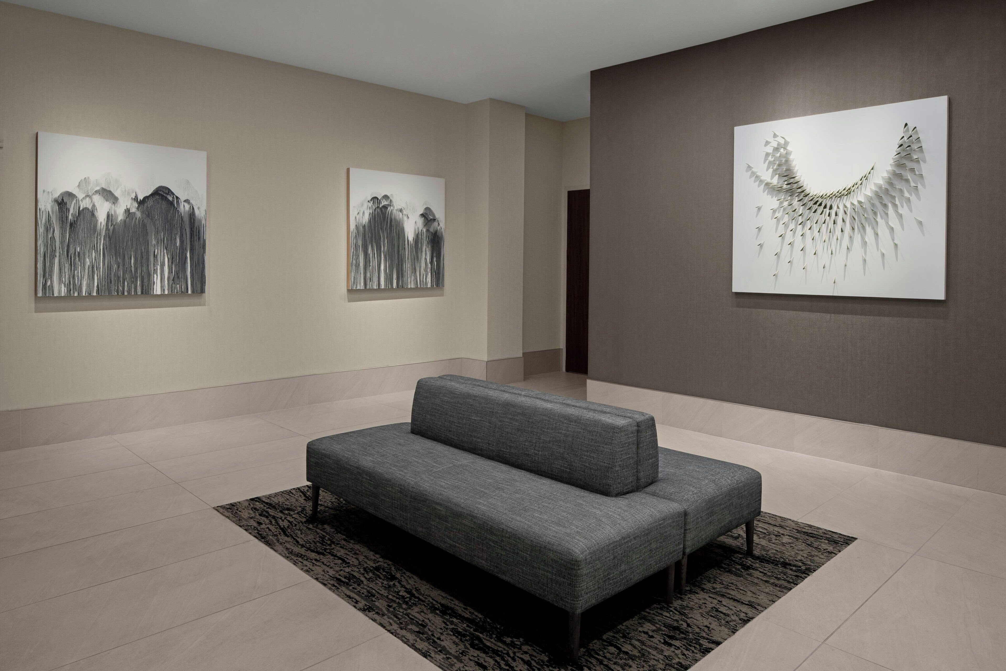 A modern art gallery with minimalist decor, featuring a grey sofa and abstract paintings on the walls.