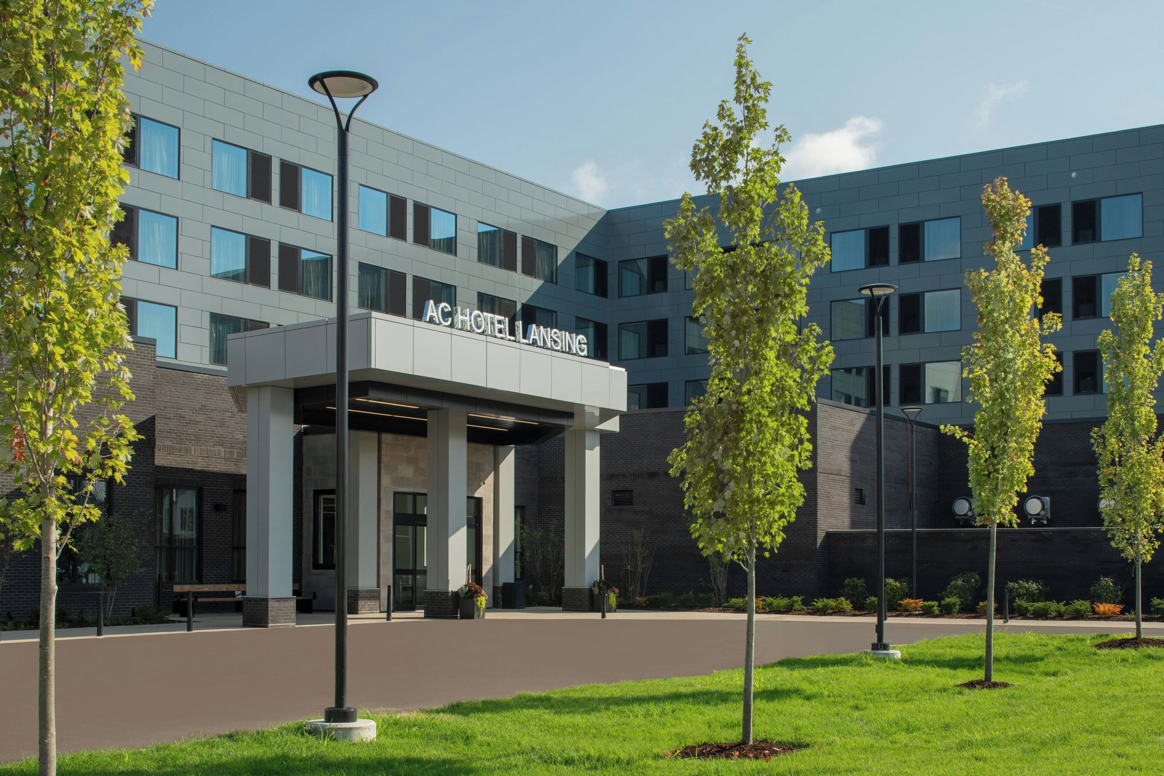 A modern hotel entrance with a covered walkway, columns, and a sign reading "AC HotelLansing".