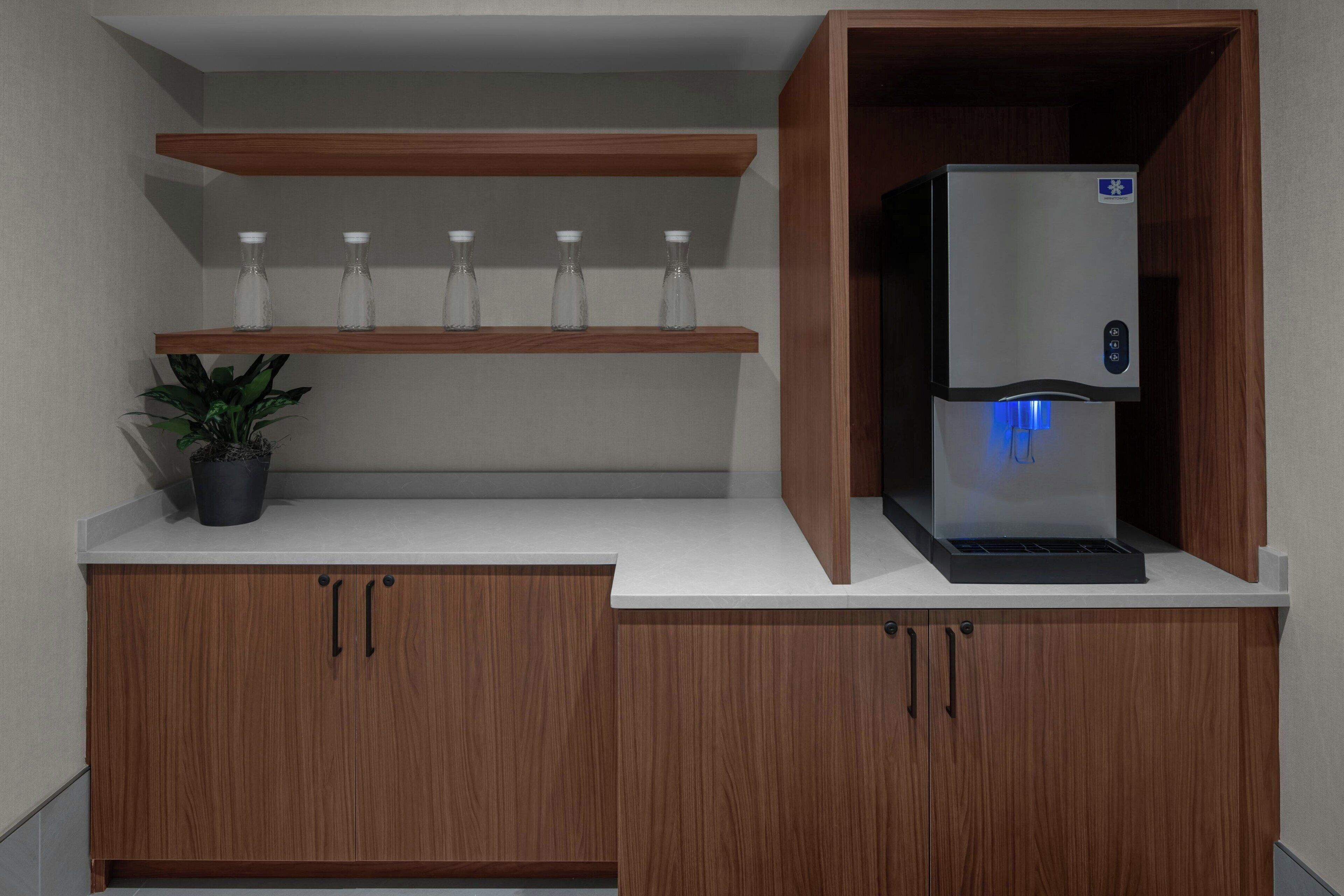 A kitchenette with a built-in refrigerator, a shelf with glass bottles, and a potted plant.
