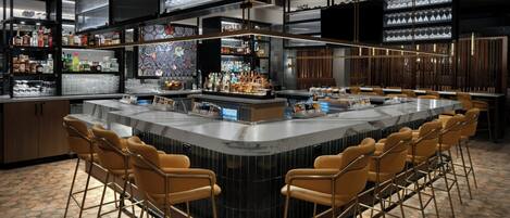 A modern bar area with a central island, bar stools, and shelves stocked with bottles and glasses.