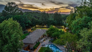 Una propiedad residencial con piscina, un patio cubierto y vistas a un área boscosa.