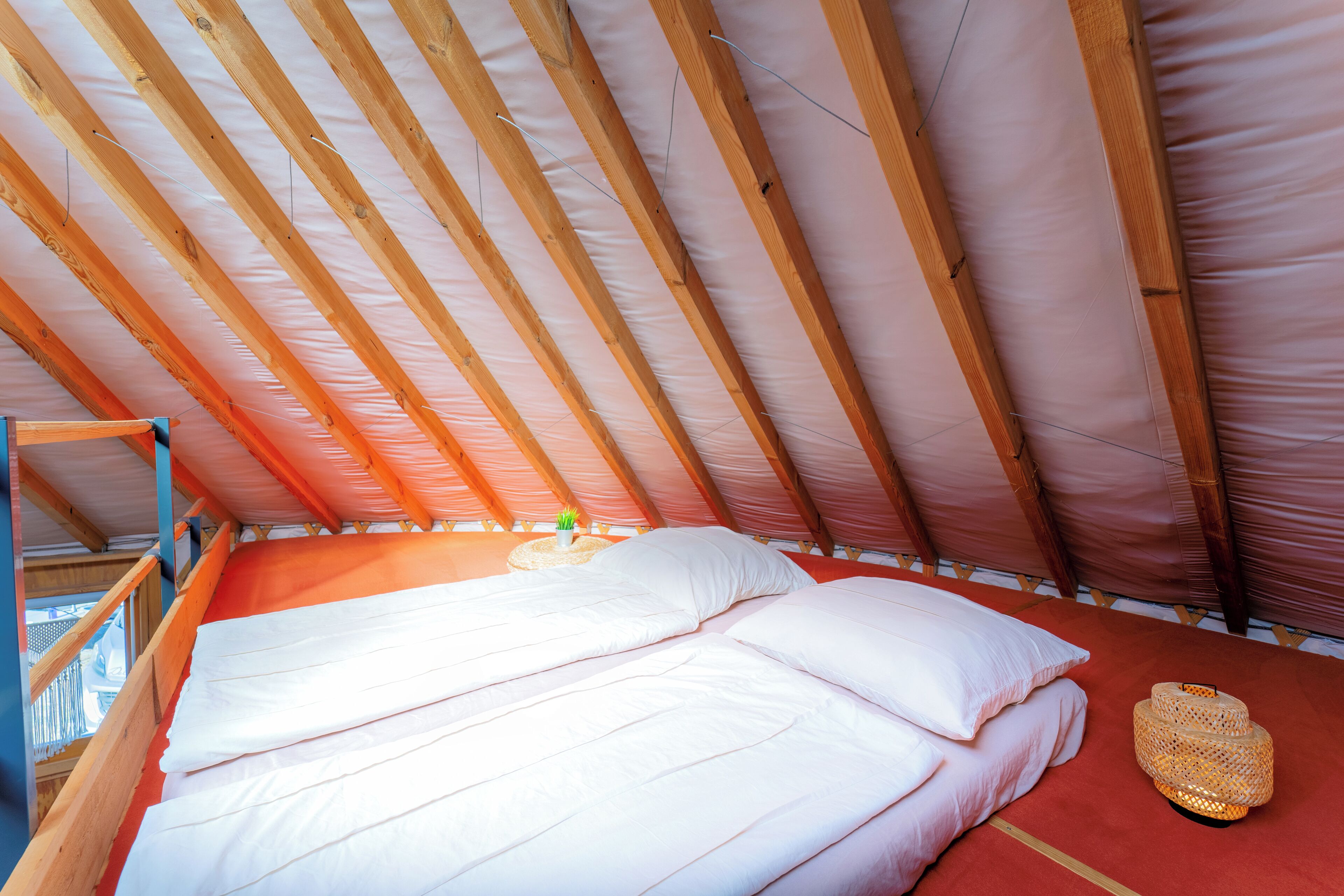 Ein Einzelbett mit weißer Bettwäsche in einem Raum mit schrägem Dach und Holzbalken.