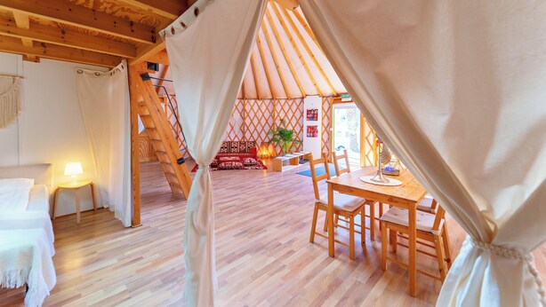 Ein gemütliches Interieur mit Holzboden, einer Essecke mit Stühlen, einem Tisch und einem Bett mit Lampe.