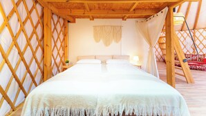 Ein gemütliches Zimmer mit Holzbalkendecke, einem Bett mit weißer Bettwäsche und einem kleinen Nachttisch mit Lampe.