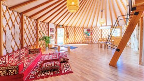 Ein geräumiges Jurten-Innendesign mit einer zentralen Sitzgruppe, Holzbalken und einer hängenden Leuchte.