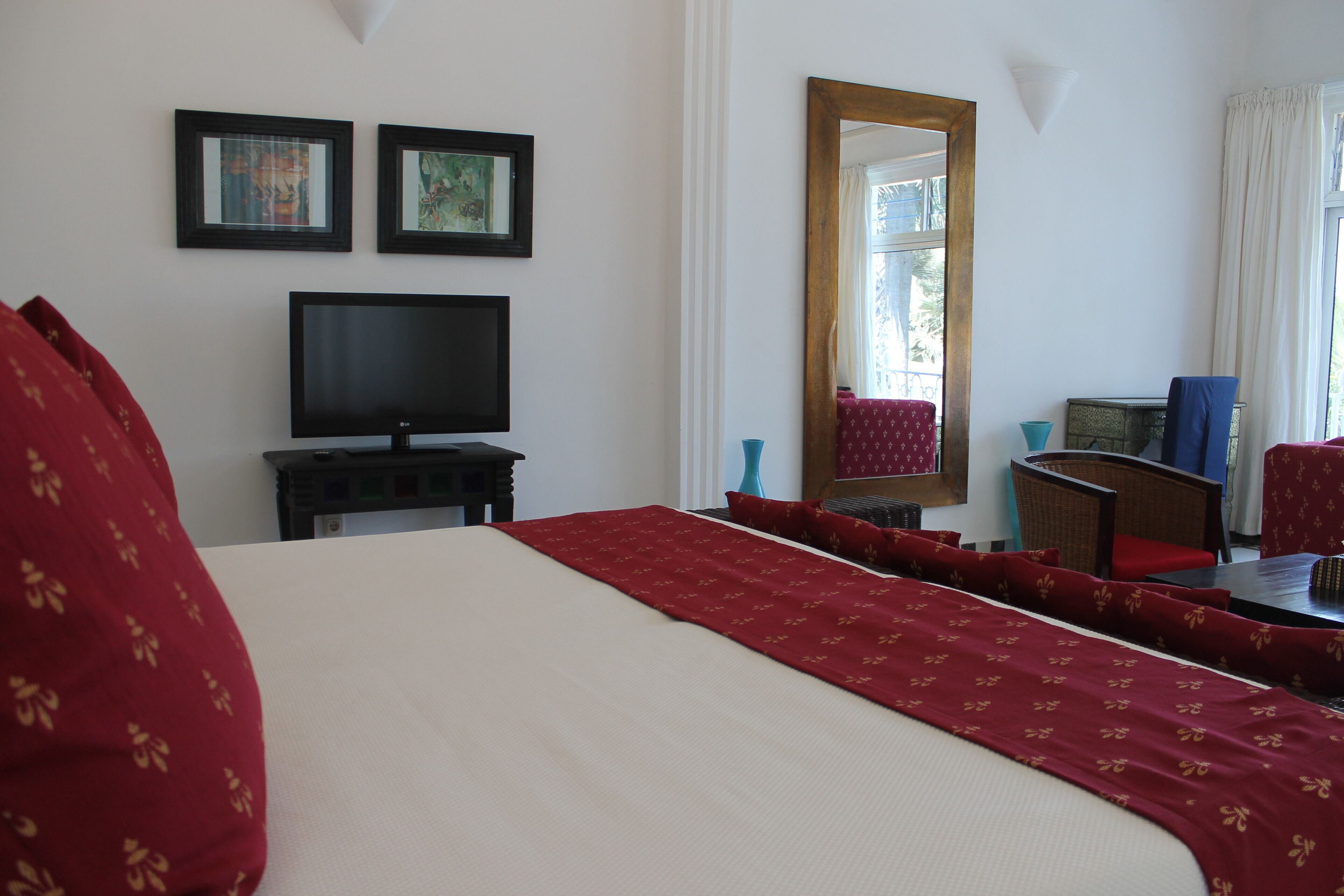 A hotel room with a large bed, a television, a desk with a chair, and a window with curtains.