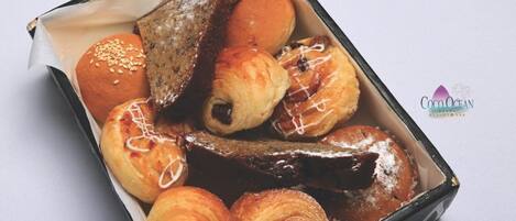 Una caja de pasteles variados, incluyendo croissants, un éclair de chocolate y un bollo glaseado.