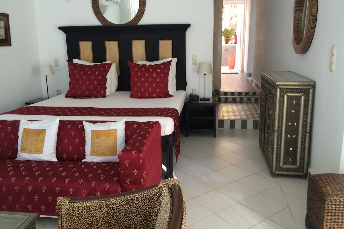 A hotel room with a large bed, two bedside tables, a nightstand, a dresser, and a mirror on the wall.