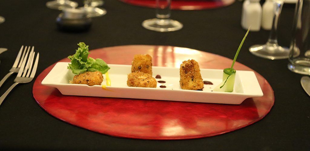 Un plato blanco rectangular con cuatro porciones de comida sobre un mantel individual rojo.