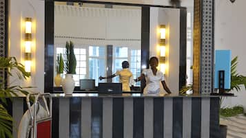 Zona reception di un hotel con banco accettazione, un grande specchio e un pavimento a righe bianche e nere.