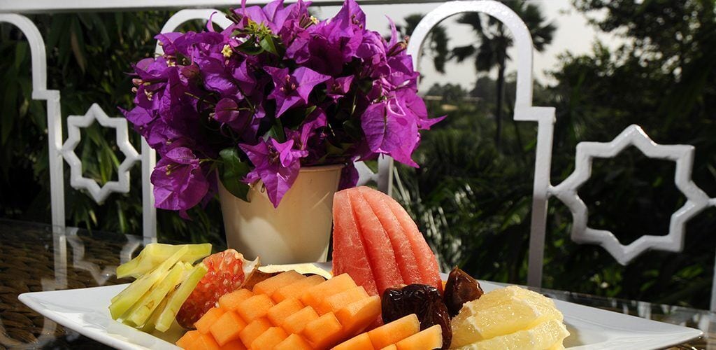 A plate of assorted fruits and a potted plant with purple flowers.