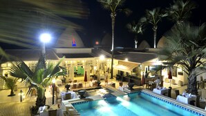 Un hotel con piscina, zona de comedor al aire libre y palmeras.