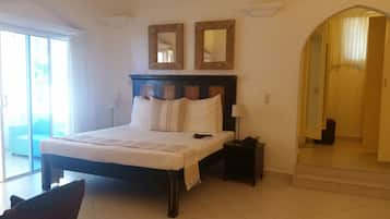 Habitación de hotel con una cama grande, dos espejos en la pared, una mesita de noche con lámpara y vistas al exterior a través de una puerta corrediza de vidrio.