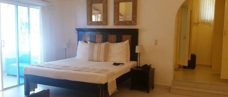 Habitación de hotel con una cama grande, dos espejos en la pared, una mesita de noche con lámpara y vistas al exterior a través de una puerta corrediza de vidrio.