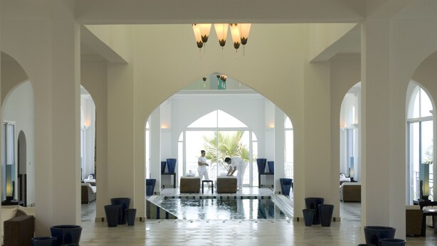Un vestíbulo amplio con piscina central, techos altos y ventanas grandes.