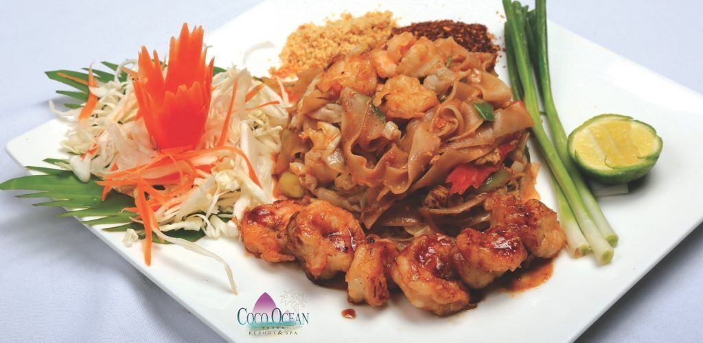 A plate of Pad Thai with shrimp, noodles, and vegetables, garnished with lime and green onions.