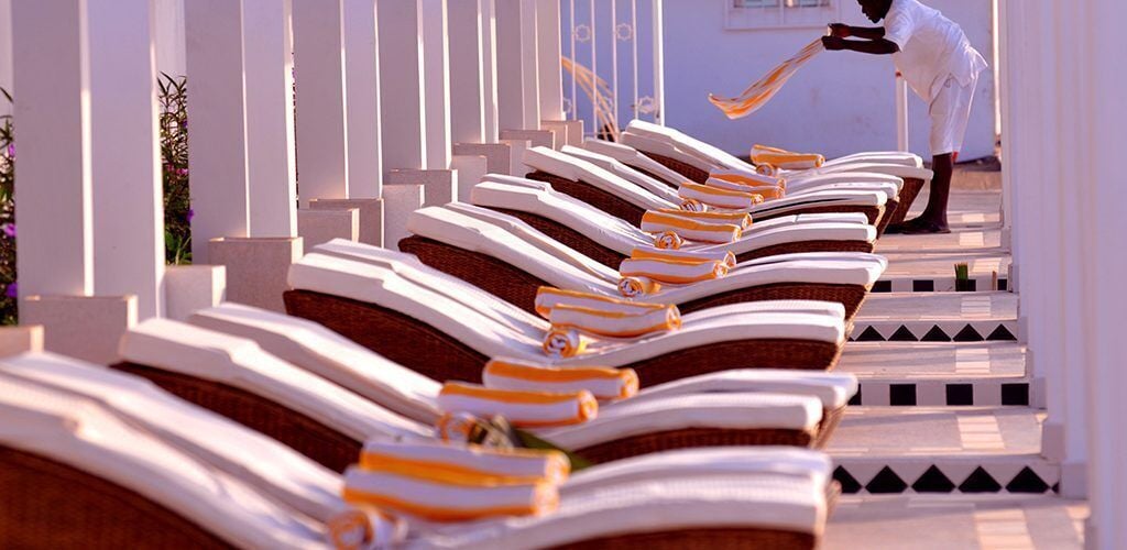 Rows of sun loungers aligned along a pathway with white pillars.