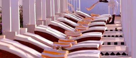 Rows of sun loungers aligned along a pathway with white pillars.