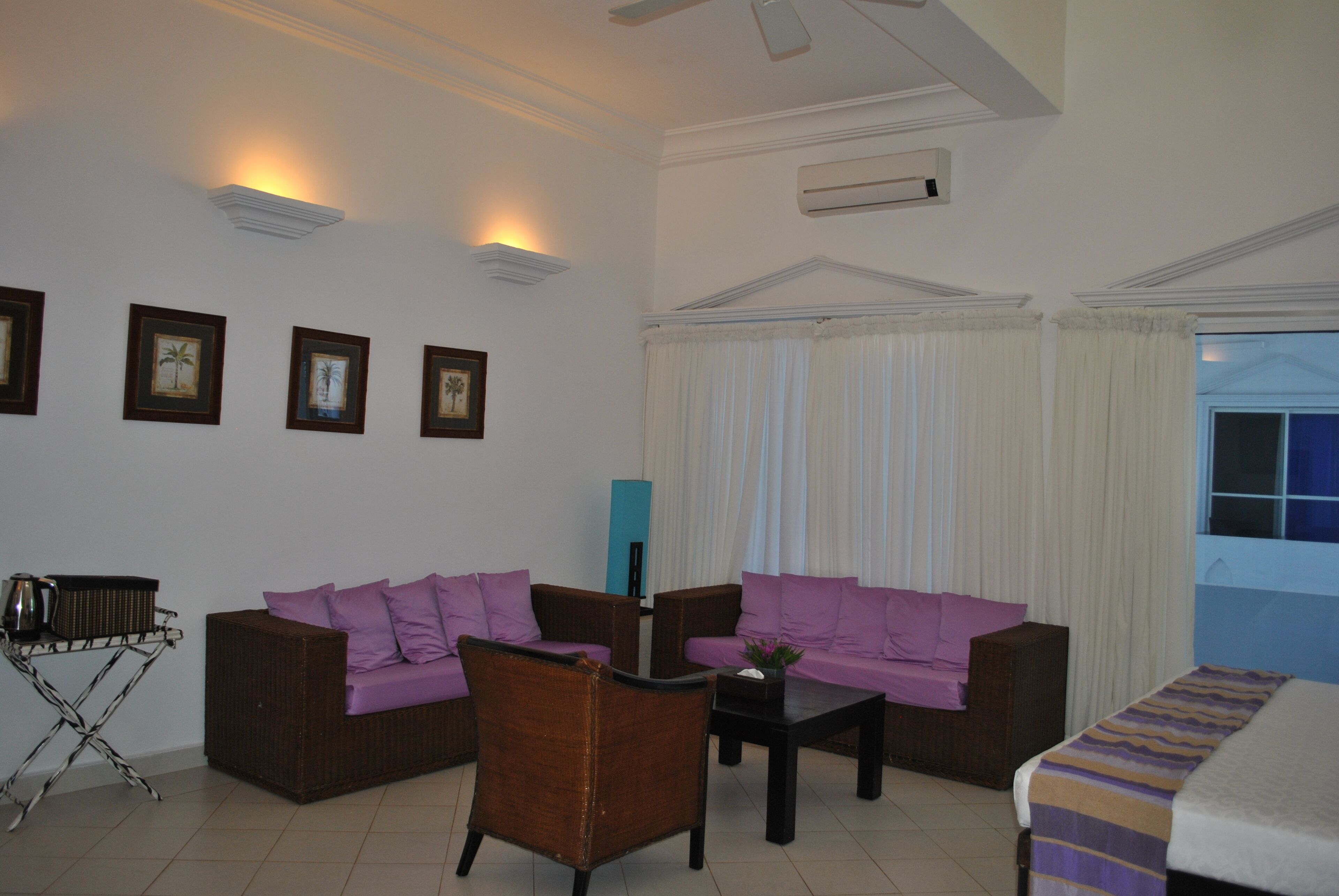 A living room with two sofas, a coffee table, and a chair. There are framed pictures on the wall and an air conditioning unit.