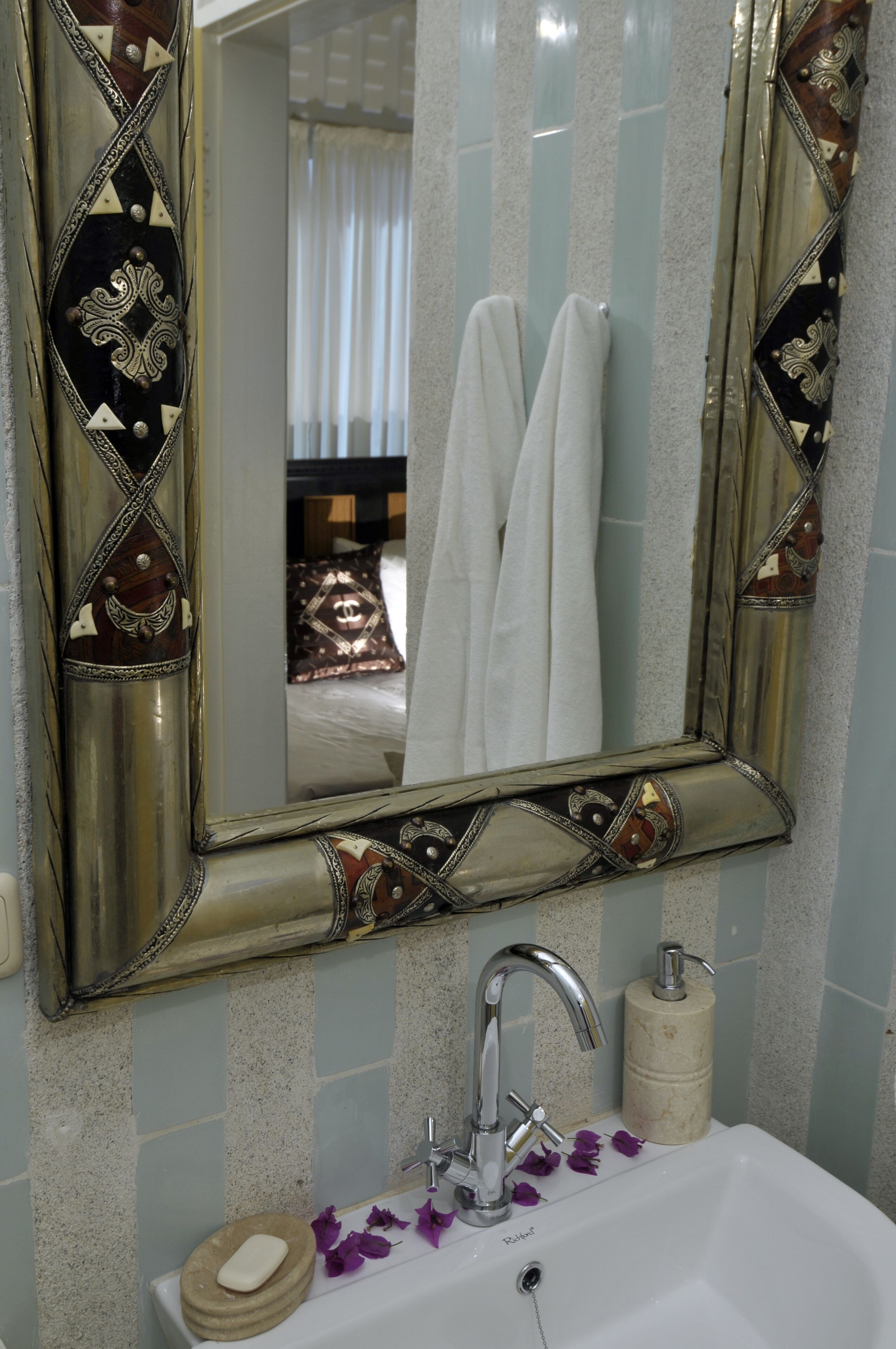 A bathroom with a decorative mirror, a sink with a soap dish, and a towel rack with white towels.