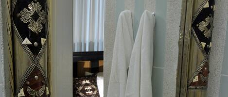 A bathroom with a decorative mirror, a sink with a soap dish, and a towel rack with white towels.
