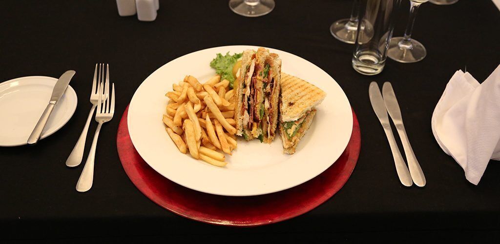 Une assiette contenant un sandwich et des frites, posée sur une table avec des couverts et des verres.