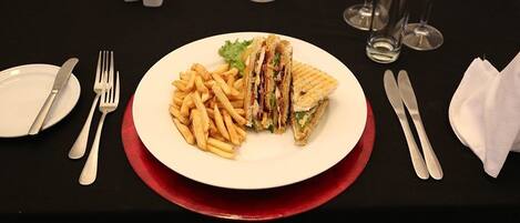 Une assiette contenant un sandwich et des frites, posée sur une table avec des couverts et des verres.
